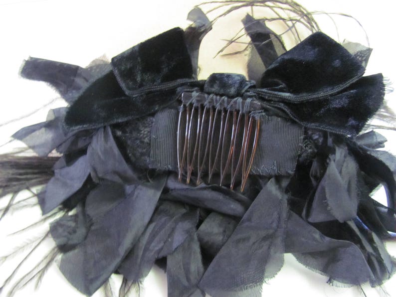 May include: A black velvet hair comb with a black feather and ribbon embellishment. The comb is decorated with a large black bow and a black feather.