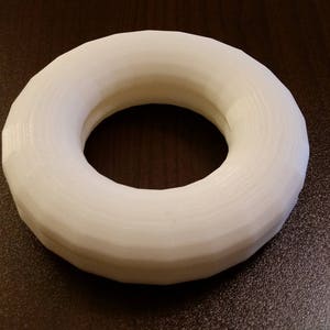 May include: A white, ring-shaped object with a hole in the center. The object has a textured surface and appears to be made of a solid material. The background is a dark brown surface.