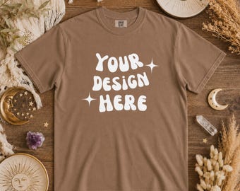以下が含まれることがあります： 「YOUR DESIGN HERE」の白文字と星のアクセントが入った茶色のTシャツ。Comfort Colorsブランドのシャツです。画像は、カスタムアパレルのための製品モックアップです。