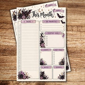 Spooky-cute printable monthly planner pages displayed on a wooden background, featuring black cats, bats, black and pink roses, crystals, moons, stars, and a mystical potion bottle. The main page includes sections for tasks, top priorities, monthly goals, events, reminders, notes, and memories.