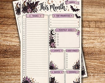 以下が含まれることがあります： This Month、Tasks、Top Priorities、Monthly Goals、Events、Don't Forget、Notes、Memoriesという文字が書かれた月間プランナーシート。黒猫、コウモリ、三日月、クリスタル、バラのイラストが描かれています。