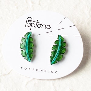 May include: A pair of green and blue leaf-shaped earrings on a white card with the text "Poptone.co".