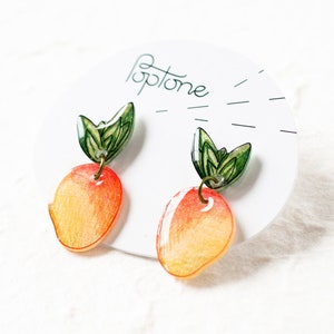 May include: A pair of peach-colored earrings with green leaves. The earrings are made of resin and have a hand-painted look. The earrings are labeled "Toptone".
