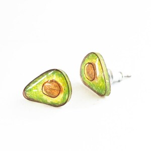 Puede incluir: Un par de pendientes con forma de aguacate con un dise&ntilde;o verde y marr&oacute;n. Los pendientes est&aacute;n hechos de resina y tienen un poste de plata.