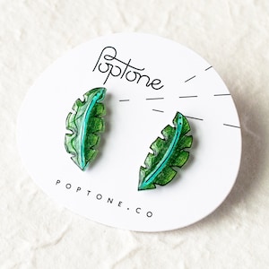 May include: A pair of green and blue leaf-shaped earrings with a white background. The earrings are made of resin and have a glossy finish. The text "Poptone.co" is printed on the background.