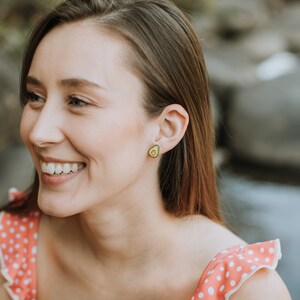 Puede incluir: Una mujer con el pelo largo y casta&ntilde;o sonr&iacute;e y lleva una blusa de lunares rosa y blancos. Lleva pendientes con forma de aguacate.