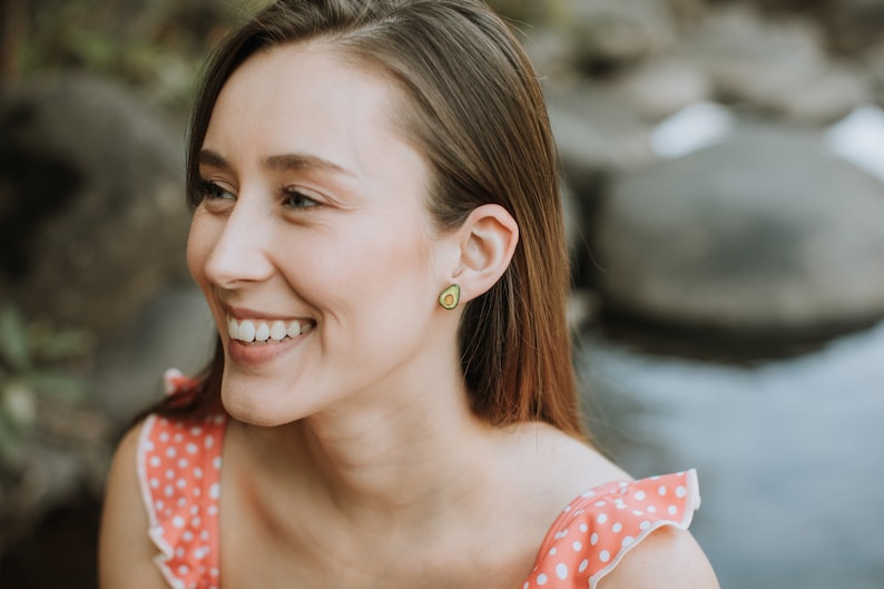 Puede incluir: Una mujer con el pelo largo y casta&ntilde;o sonr&iacute;e y lleva una blusa de lunares rosa y blancos. Lleva pendientes con forma de aguacate.