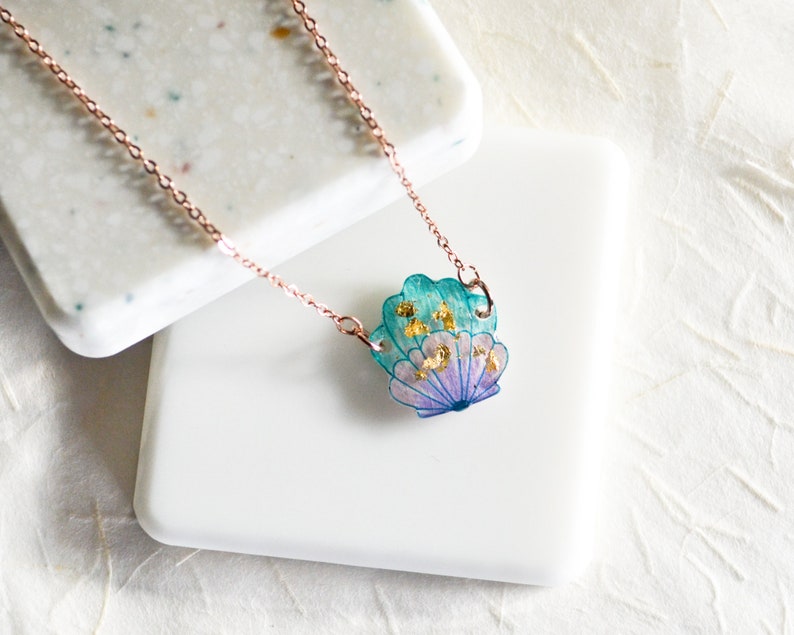 May include: A delicate rose gold chain necklace with a teal, purple, and gold seashell pendant. The seashell has a layered, iridescent look with flecks of gold.