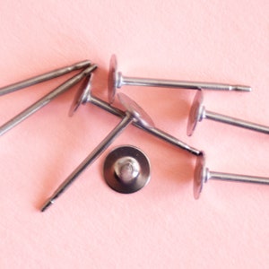 May include: A close-up of six silver earring posts with round backs. The posts are scattered on a pink surface.