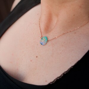 May include: A delicate rose gold chain necklace with a small, blue and green enamel flower pendant.