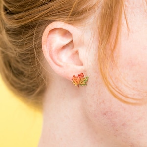 Puede incluir: Un par de pendientes con un dise&ntilde;o de hoja de arce de colores. Las hojas son un degradado de rojo, naranja, amarillo y verde.