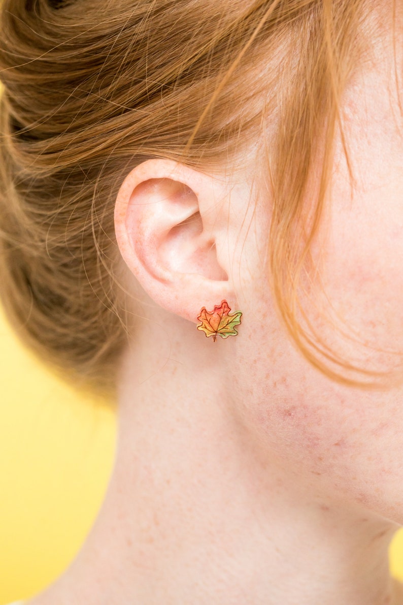 Puede incluir: Un par de pendientes con un dise&ntilde;o de hoja de arce de colores. Las hojas son un degradado de rojo, naranja, amarillo y verde.