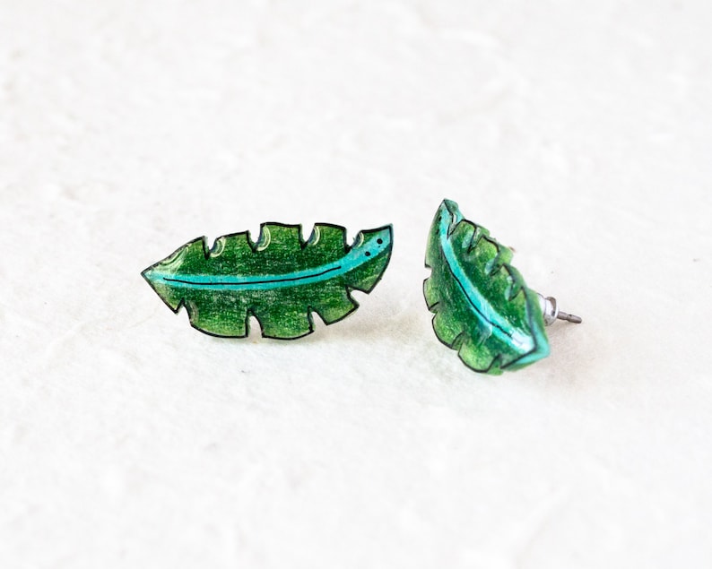 May include: A pair of green leaf-shaped earrings with a black outline and a turquoise stripe. The earrings are made of resin and have a post back.