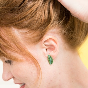 May include: A woman with red hair wearing a pair of green leaf-shaped earrings.
