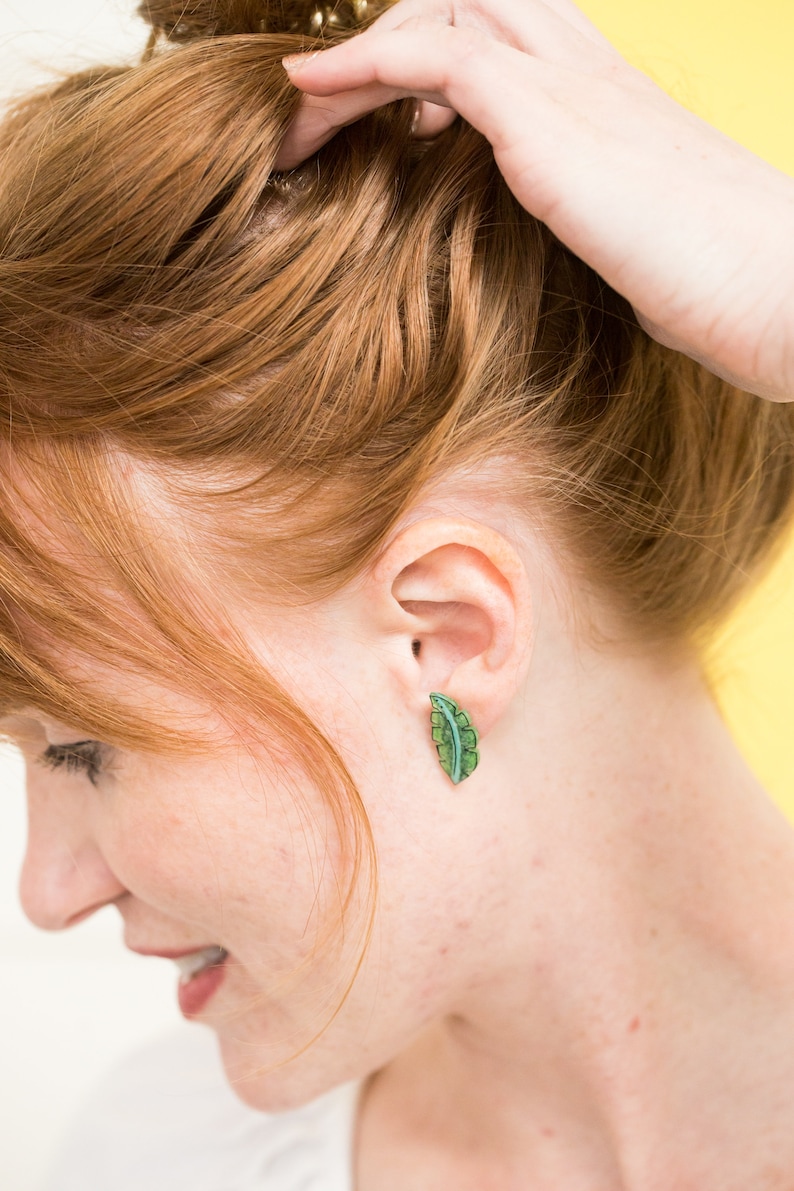 May include: A woman with red hair wearing a pair of green leaf-shaped earrings.