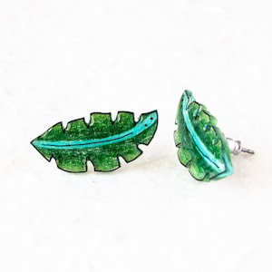 May include: A pair of green leaf-shaped earrings with a blue line down the center. The earrings are made of resin and have a post back.
