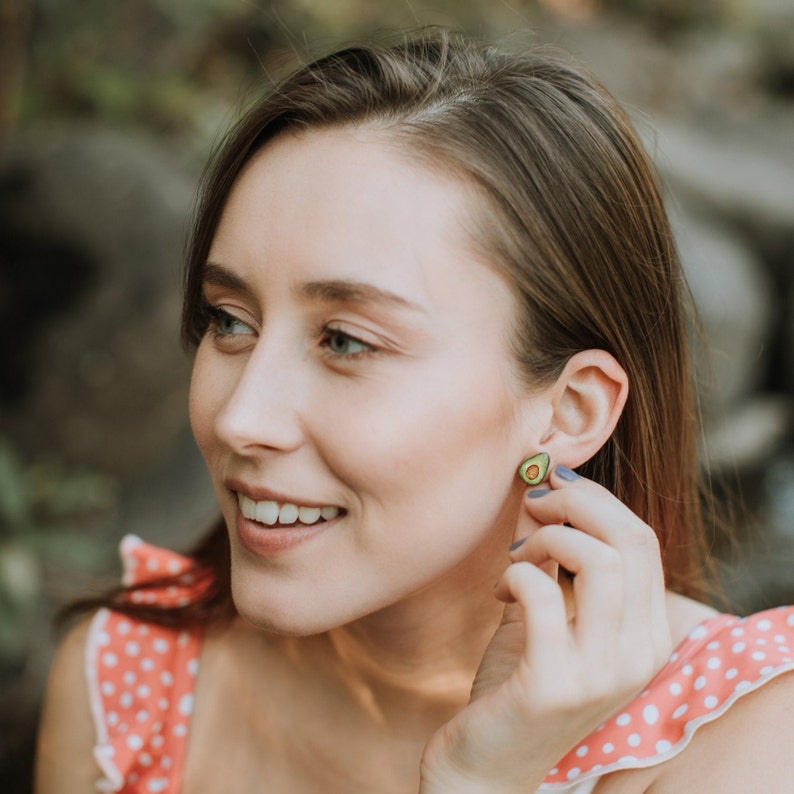 Puede incluir: Una mujer con el pelo largo y casta&ntilde;o lleva un vestido de lunares rosa y blanco. Est&aacute; sonriendo y mirando hacia un lado. Lleva un peque&ntilde;o pendiente en forma de aguacate en la oreja derecha.