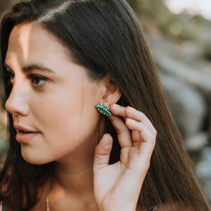 May include: A woman wearing a green leaf necklace and earrings. The earrings are small and shaped like leaves. The necklace is a delicate chain with a larger leaf pendant.