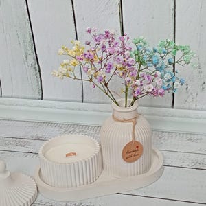 Puede incluir: Un juego de velas y jarrones de cerámica blanca con una bandeja, con una vela con una mecha de madera y un jarrón con flores secas de colores. El jarrón tiene una etiqueta que dice "Handmade with love".