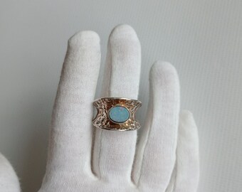 Puede incluir: Un anillo de plata con una banda texturizada y una piedra de ópalo ovalada azul claro.