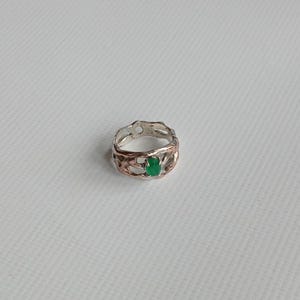 May include: A silver ring with a green gemstone set in a textured band. The ring has a unique, organic design.