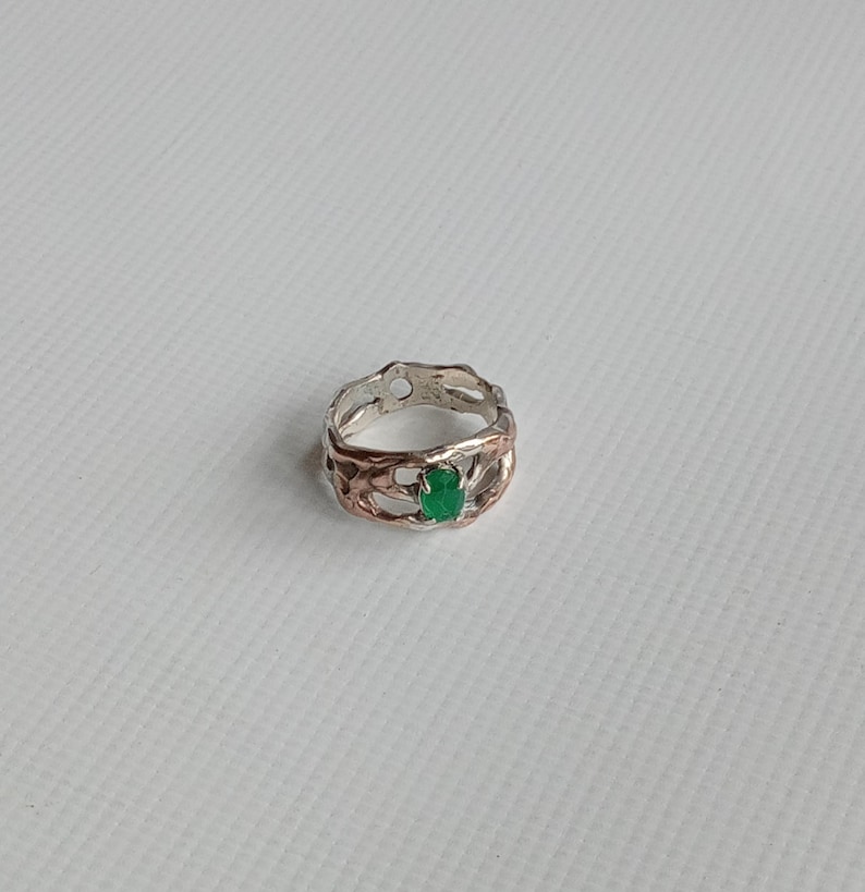 May include: A silver ring with a green gemstone set in a textured band. The ring has a unique, organic design.