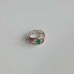May include: A silver ring with a green gemstone set in a delicate, intricate design.