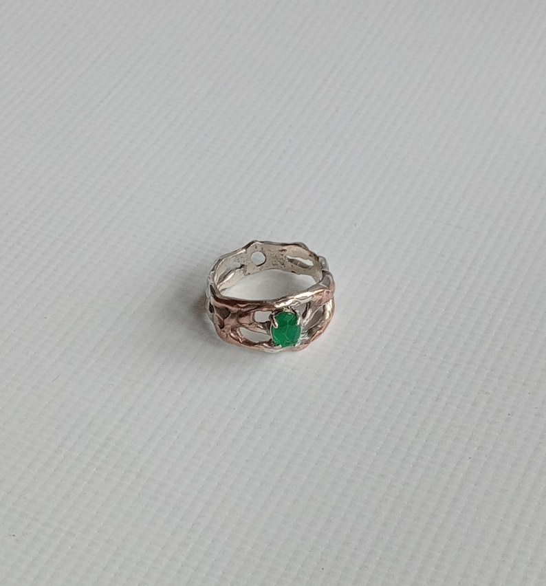 May include: A silver ring with a green gemstone set in a delicate, intricate design.