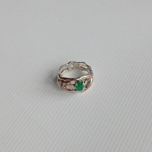 May include: A silver ring with a green gemstone set in a delicate, intricate design.