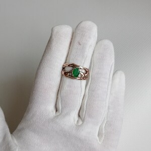 May include: A rose gold ring with a green oval gemstone set in a delicate, wavy band.