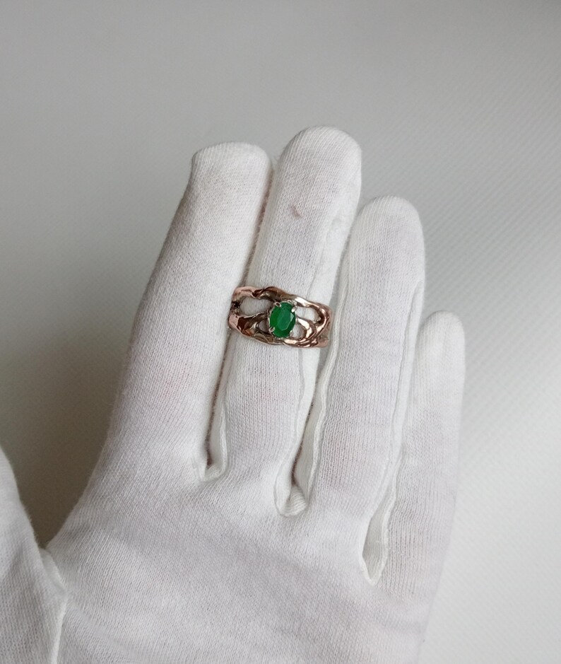 May include: A rose gold ring with a green oval gemstone set in a delicate, wavy band.