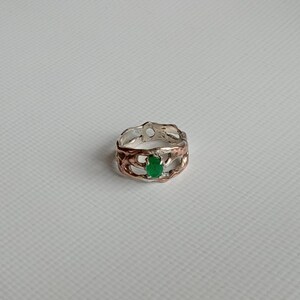 May include: A silver and copper ring with a green gemstone set in the center. The ring has a unique, organic design.