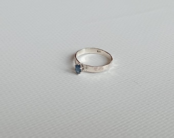 May include: A silver ring with a hammered texture and a small blue gemstone.