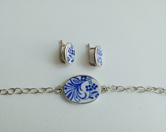 May include: A silver chain bracelet with a blue and white porcelain oval charm. The charm features a floral design. Matching blue and white porcelain earrings with floral designs are also included.