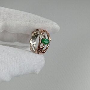 May include: A silver and rose gold ring with a green gemstone set in a delicate, intricate design.