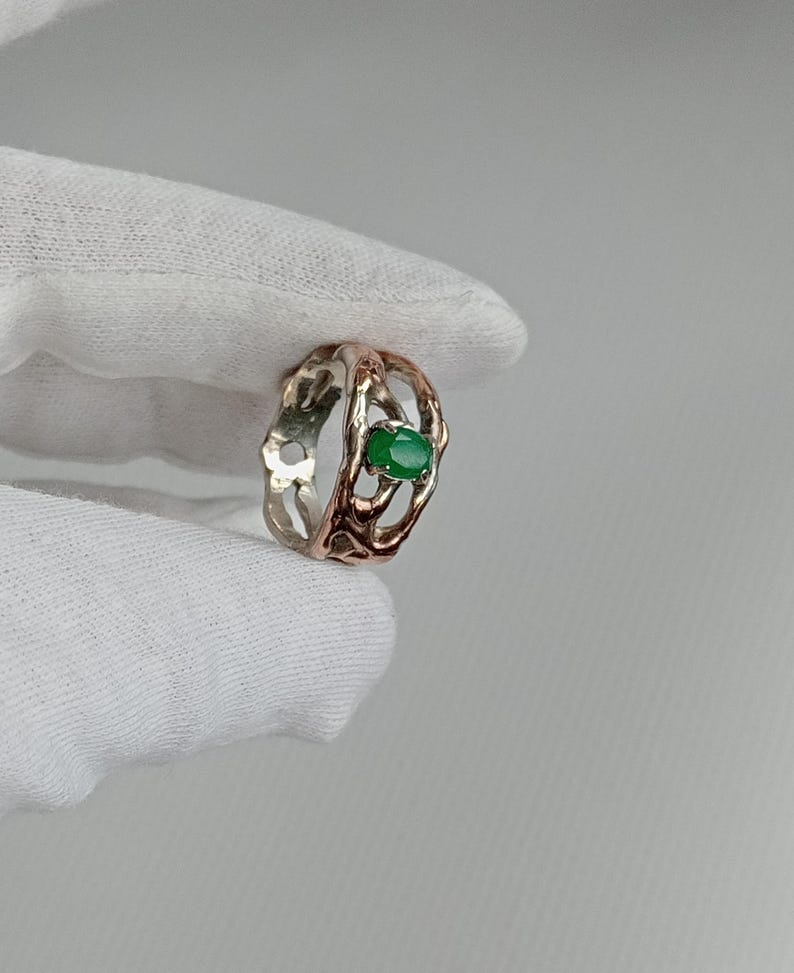 May include: A silver and rose gold ring with a green gemstone set in a delicate, intricate design.