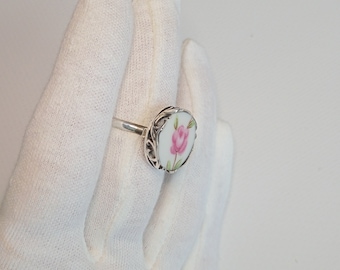 May include: A silver ring with a white porcelain setting featuring a pink rose design.