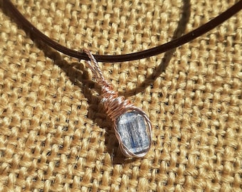 Puede incluir: Un colgante de alambre plateado con un cristal transparente facetado en un cordón de cuero marrón.