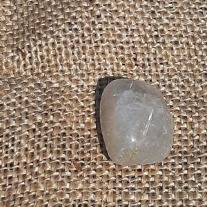 以下が含まれることがあります： 茶色の麻布の背景に、金色の内包物を含む透明な水晶。ルチルクォーツとしても知られています。