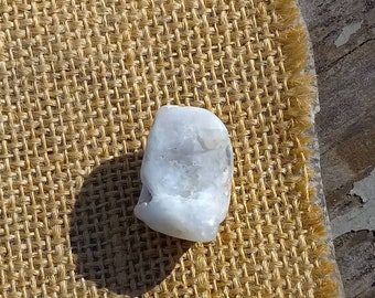 May include: A white, opaque, smooth, rounded, natural stone on a brown burlap background.