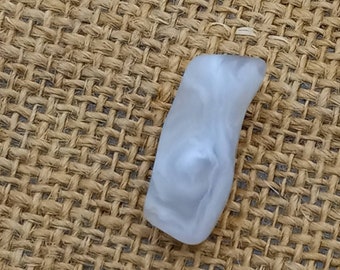May include: A white, opaque, smooth, and slightly curved stone with a swirling pattern. The stone is sitting on a brown burlap surface.
