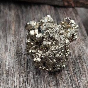 Peut inclure: Un amas de cristaux de pyrite bruts de couleur dorée, également appelés or des fous, sur une surface en bois brun rugueuse.