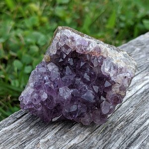 May include: A cluster of amethyst crystals in shades of purple and white. The crystals are arranged in a natural formation, creating a unique and beautiful piece.
