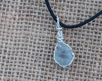 May include: A silver wire wrapped pendant featuring a clear, faceted gemstone on a black cord necklace.