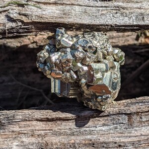 May include: A large, metallic, gold-colored pyrite crystal cluster with a rough, textured surface. The crystal is sitting on a piece of weathered wood.