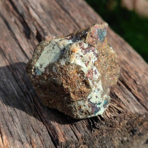 May include: A rough, irregularly shaped rock with a mix of brown, gray, and white colors. The rock has a metallic sheen and appears to be a type of mineral.