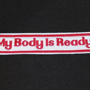 May include: A white embroidered patch with a red border and the text "My Body Is Ready" in red, centered on the patch. The patch is rectangular with rounded corners and is set against a black background.