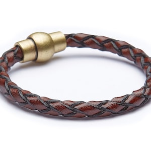 May include: A brown leather bracelet with a black braided design and a gold-toned magnetic clasp.