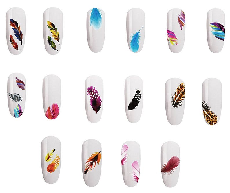 May include: A collection of white nail tips, each adorned with a unique feather design. The feathers feature a variety of colors, including blue, orange, yellow, and purple, and some have patterned details. The nail art is arranged in rows and columns.
