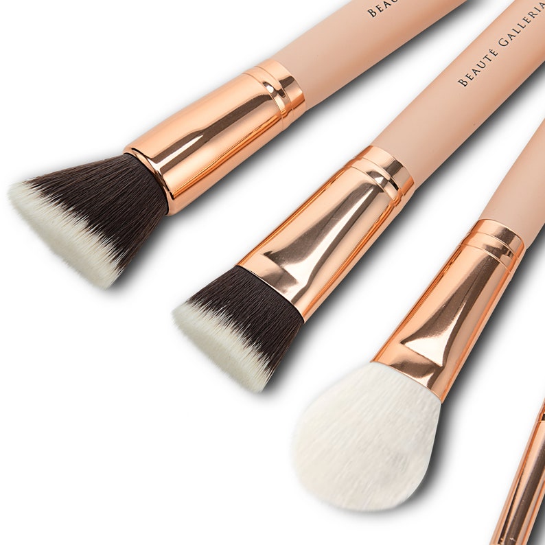 Op de afbeelding: Set van drie make-up kwasten met ros&eacute;gouden handvatten en witte borstels. De kwasten zijn gelabeld "Beaute Galleria".